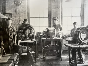 Old photograph of three men and a teen boy working in the original Rapa Electric machine shop in 1966